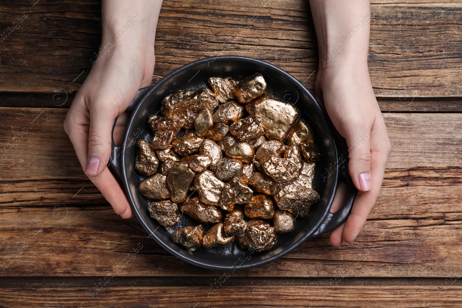 Photo of Woman with pan of gold nuggets at wooden table, top view