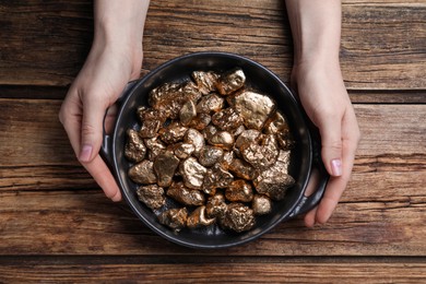 Woman with pan of gold nuggets at wooden table, top view