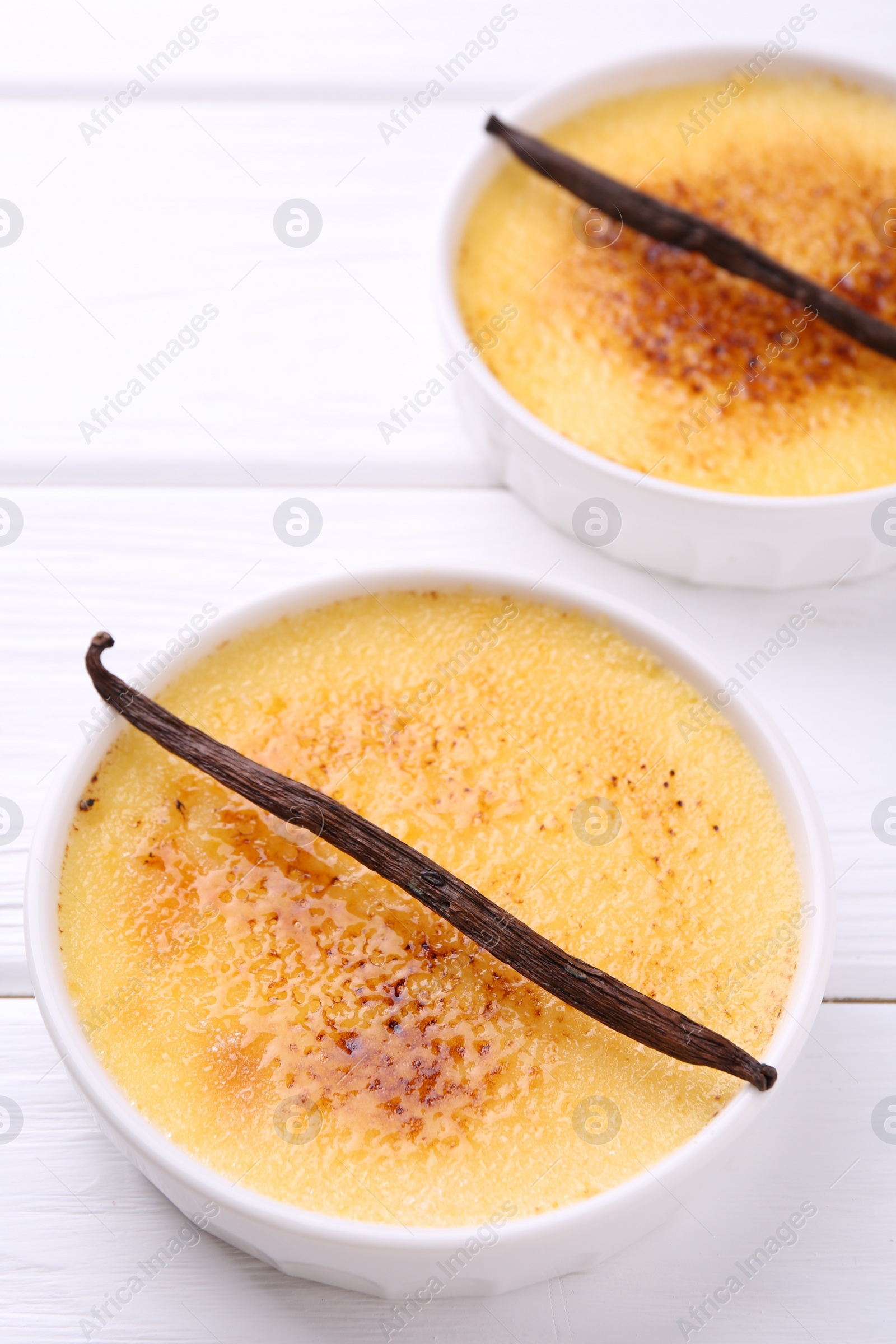 Photo of Delicious creme brulee in bowls and vanilla pods on white wooden table
