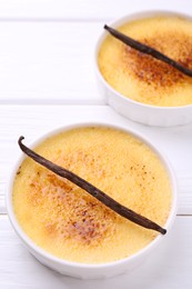 Delicious creme brulee in bowls and vanilla pods on white wooden table