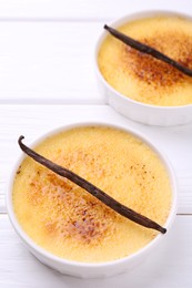 Photo of Delicious creme brulee in bowls and vanilla pods on white wooden table