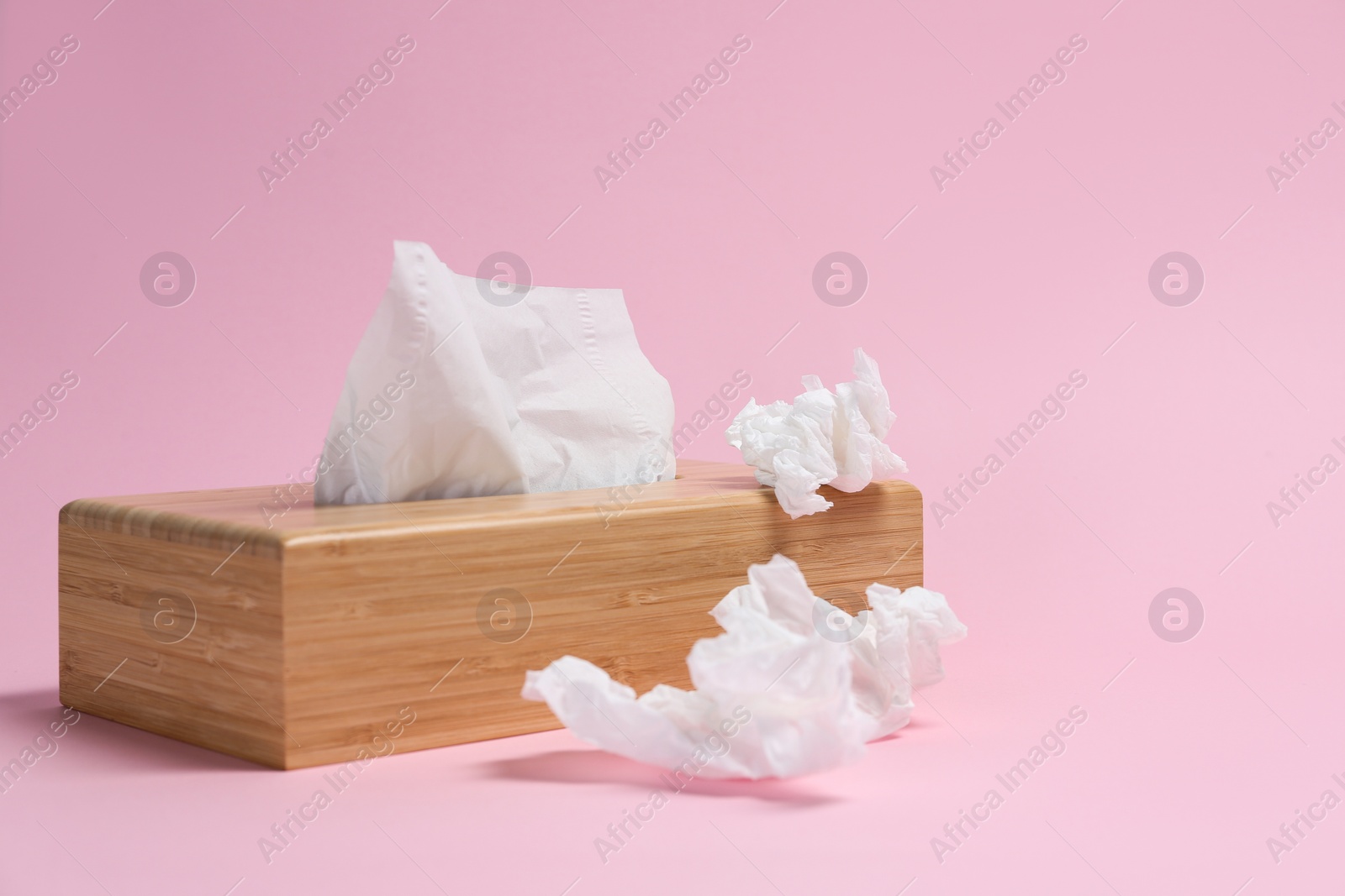 Photo of Holder with paper tissues and used crumpled napkins on pink background