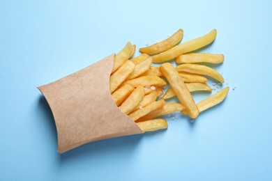 Paper cup with French fries on light blue table, flat lay