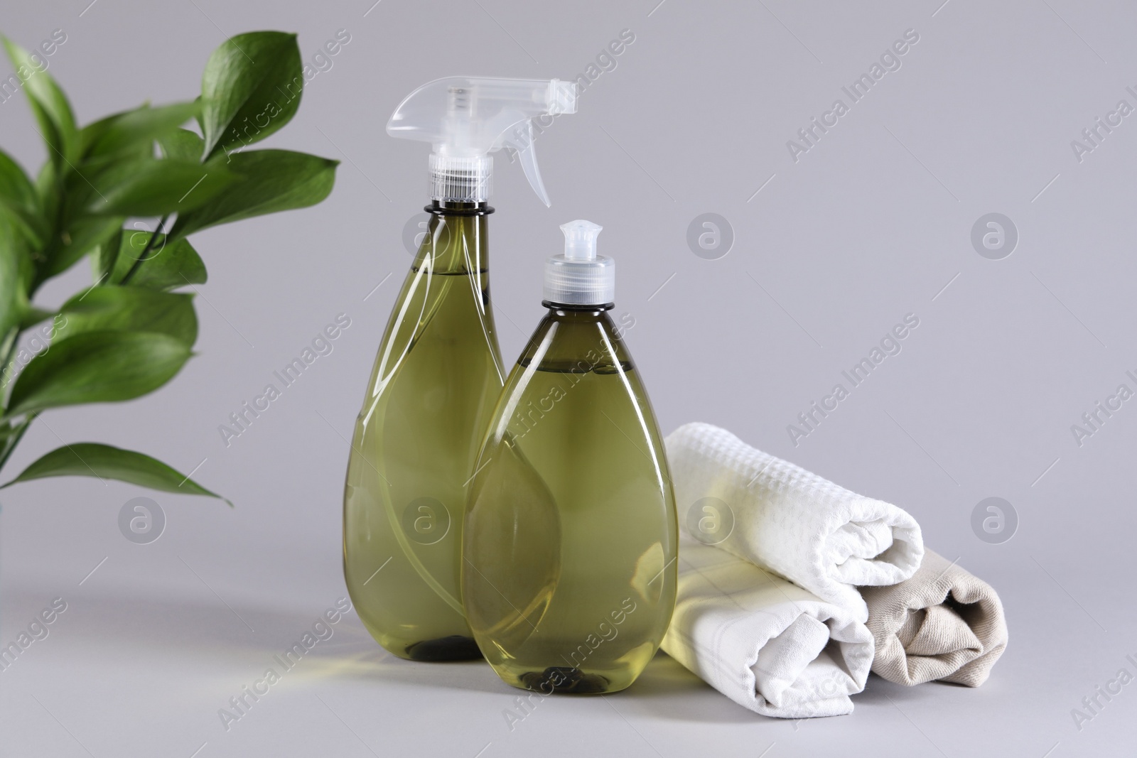 Photo of Bottles of cleaning product and rolled rags on light background