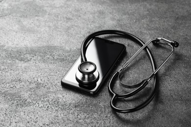 Photo of Modern smartphone and stethoscope on grey table. Space for text