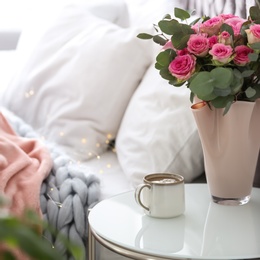 Cup of coffee and flowers on table near bed