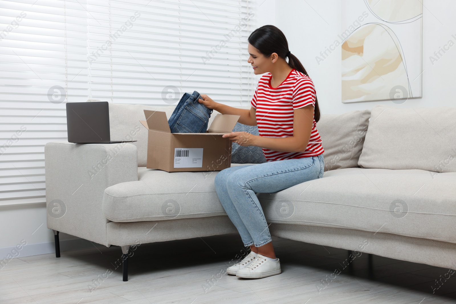 Photo of Young woman with just unpacked new jeans on sofa at home. Online shopping