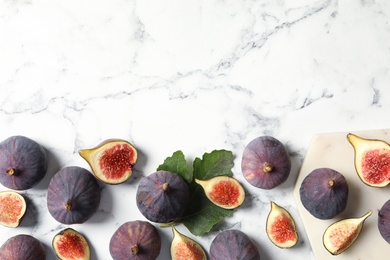 Whole and cut tasty fresh figs on white marble table, flat lay. Space for text