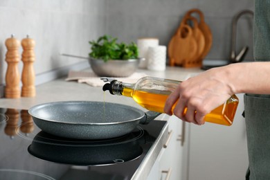 Photo of Vegetable fats. Woman pouring cooking oil into frying pan on stove in kitchen, closeup