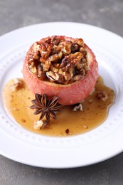 Photo of Tasty baked apple with nuts, honey and anise on gray table, closeup