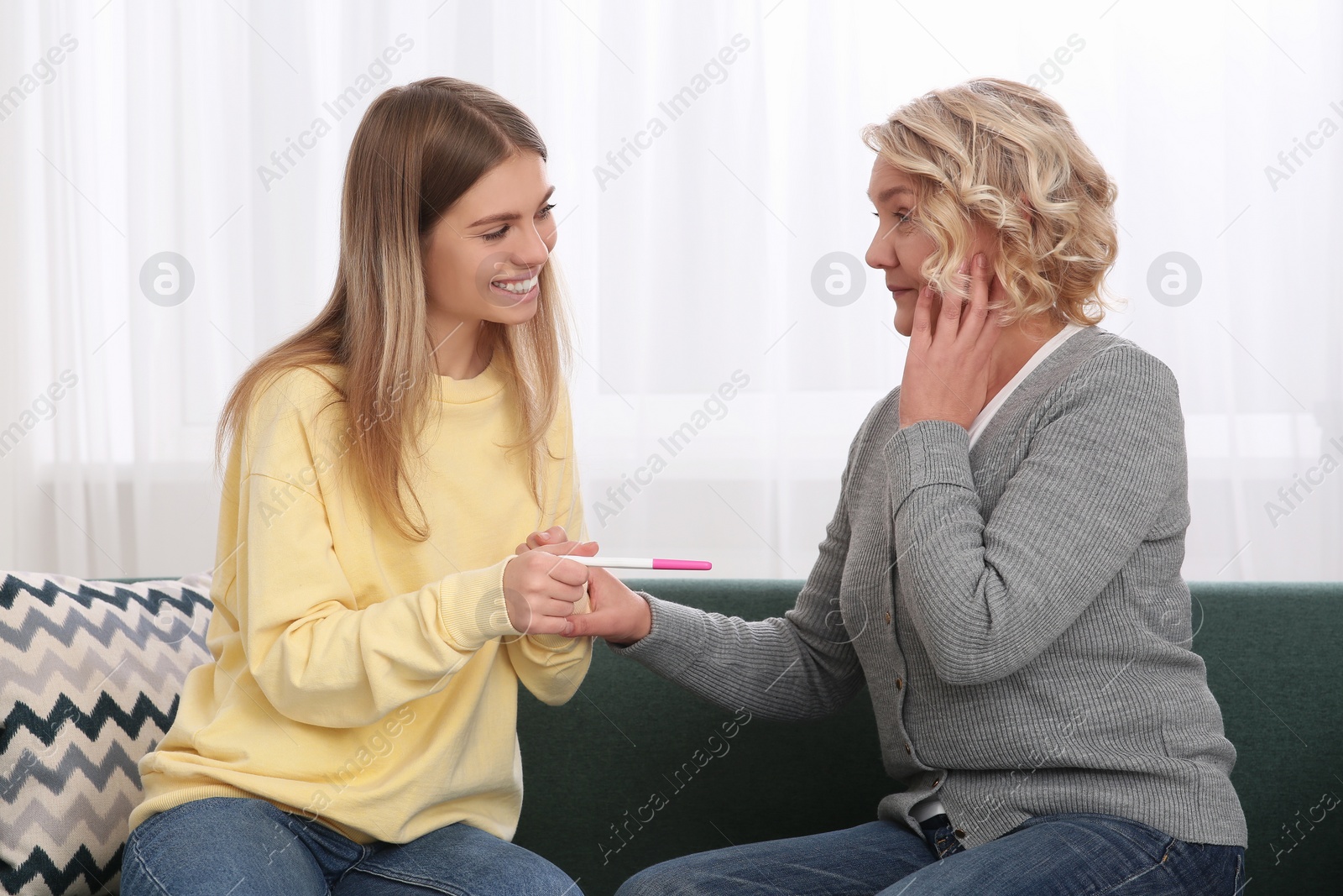 Photo of Young woman showing her mother pregnancy test at home. Grandparent reaction to future grandson