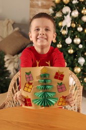Cute little child with beautiful Christmas card at table in decorated room
