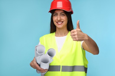 Photo of Architect in hard hat with drafts showing thumbs up on light blue background