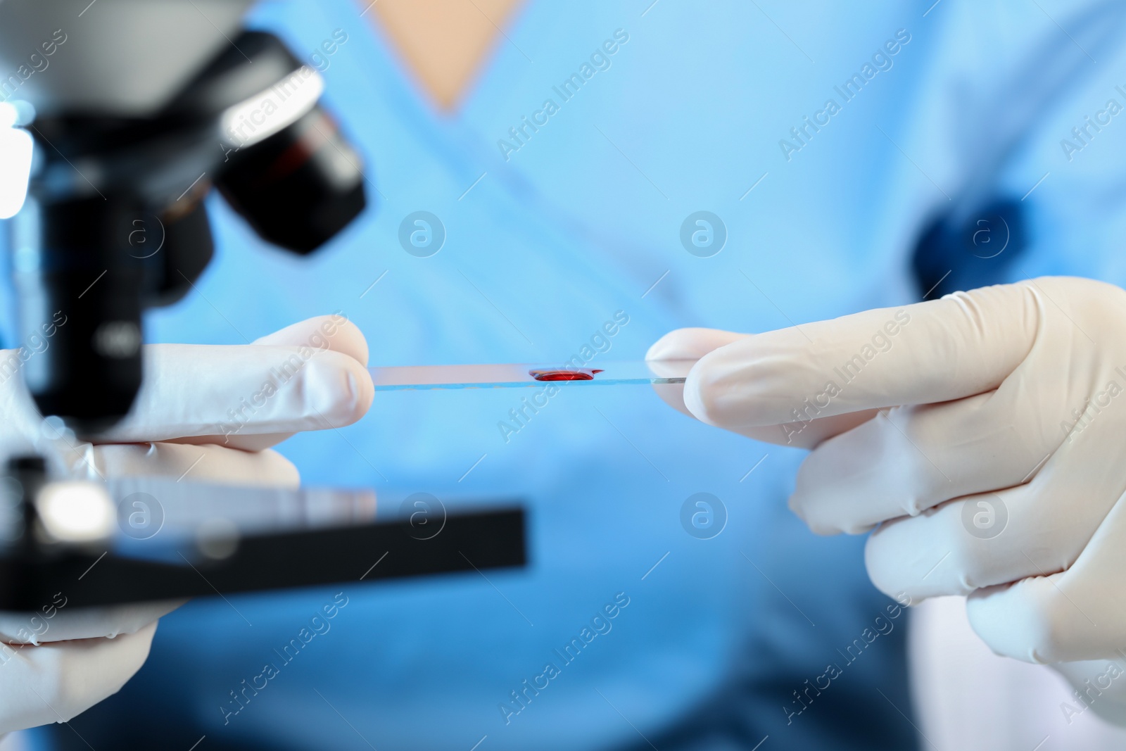 Photo of Scientist holding microscope slide with sample of red liquid in laboratory, closeup
