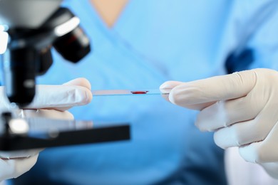 Scientist holding microscope slide with sample of red liquid in laboratory, closeup