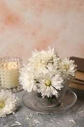 Photo of Composition of chrysanthemum flowers, books and candle on grey textured table