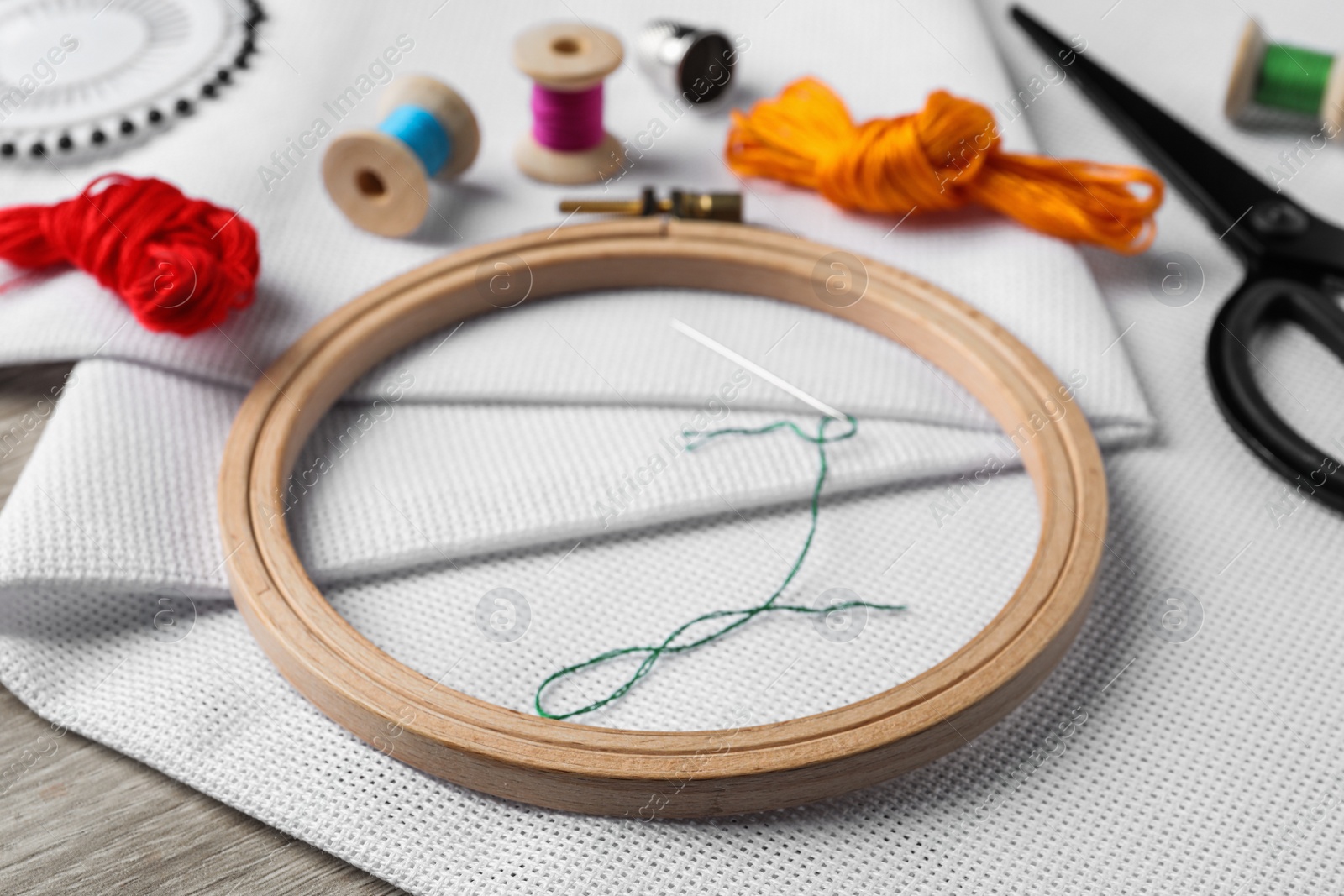 Photo of Embroidery hoop, fabric and other accessories on wooden table