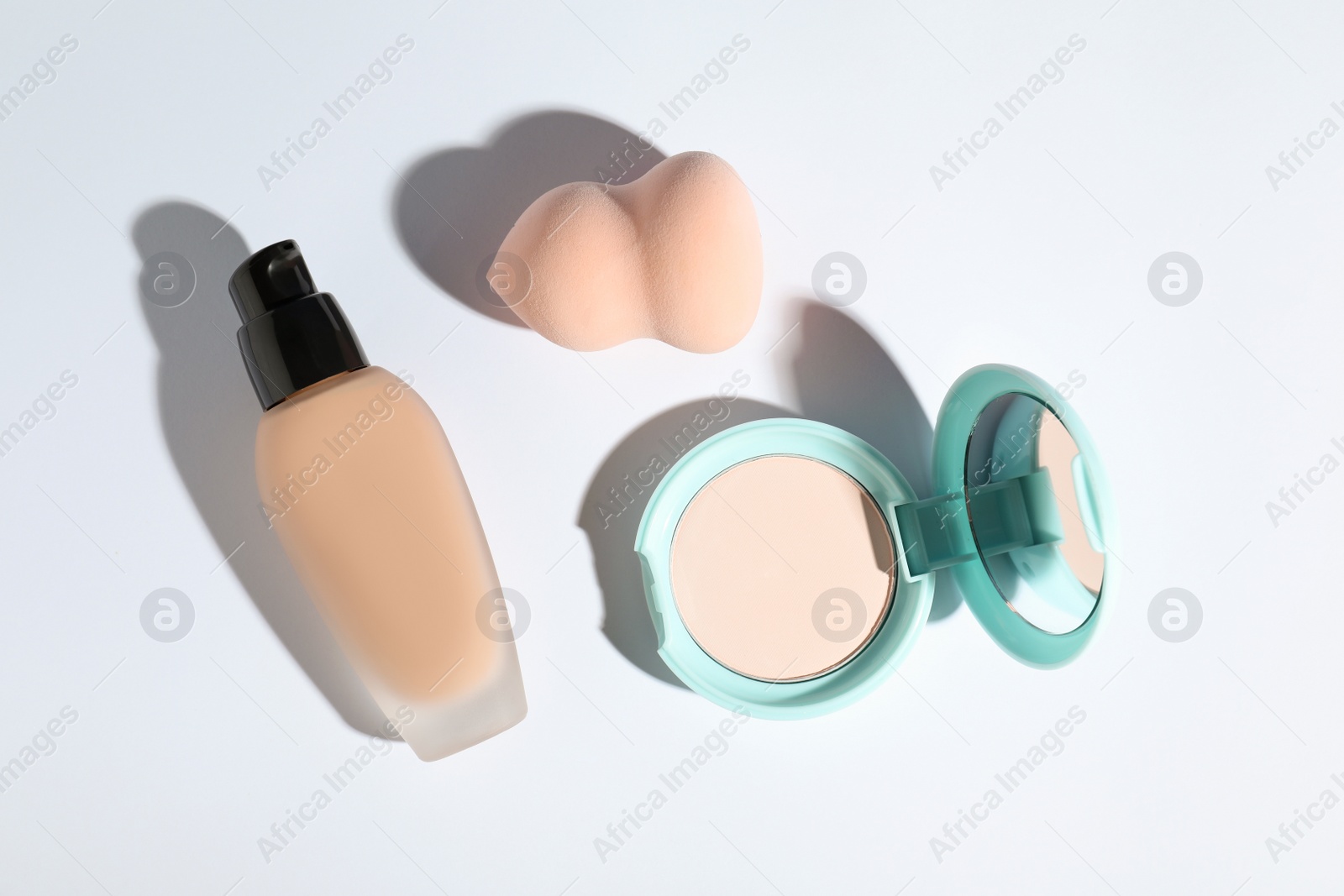 Photo of Skin foundation, powder and makeup sponge on white background, top view