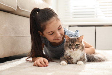 Photo of Cute little girl with cat lying on carpet at home. First pet