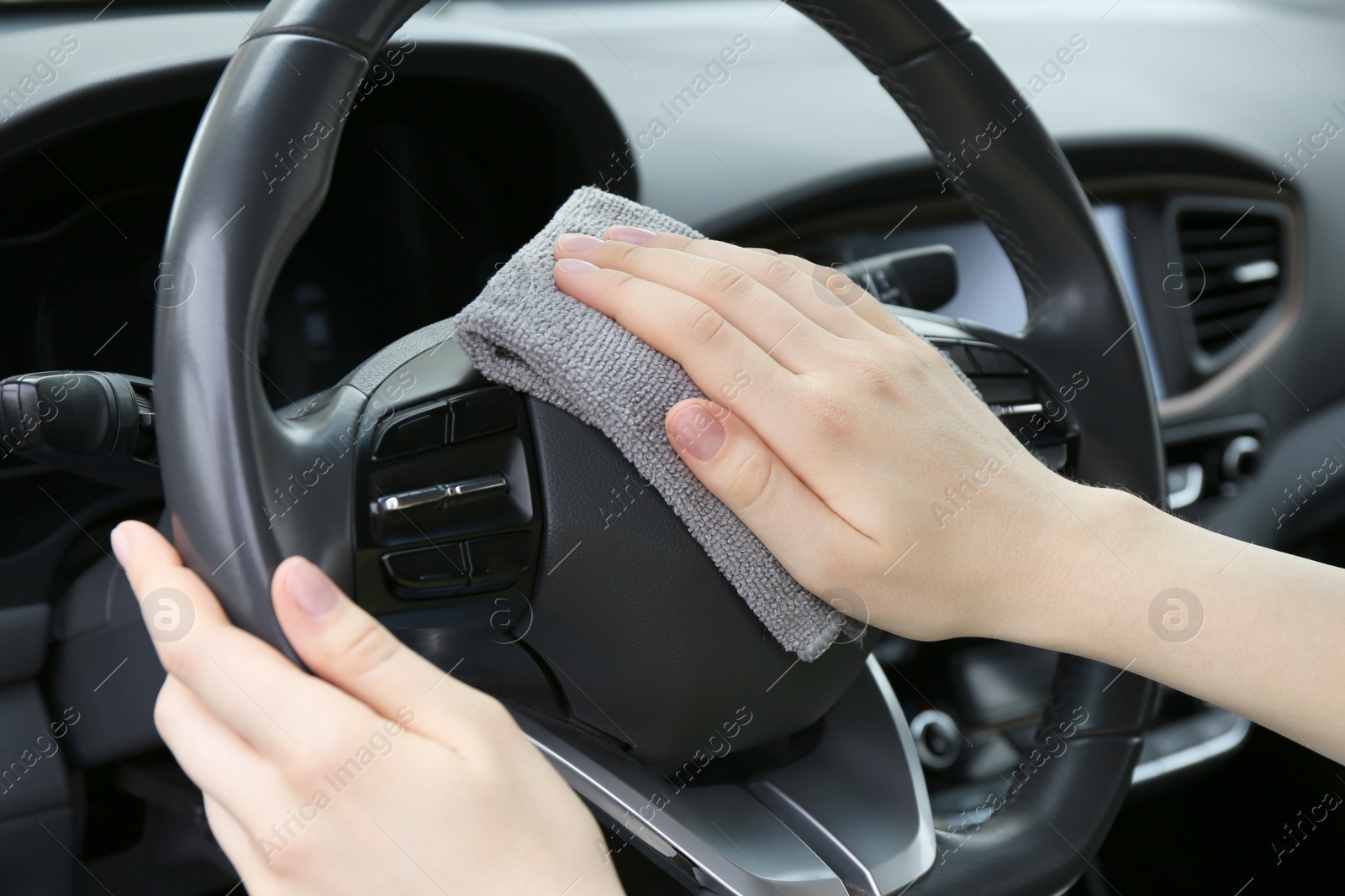 Photo of Woman cleaning steering wheel with rag in car, closeup