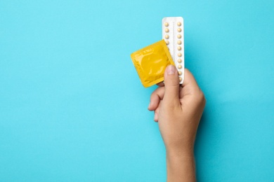 Woman holding condom and birth control pills on blue background, top view with space for text. Safe sex