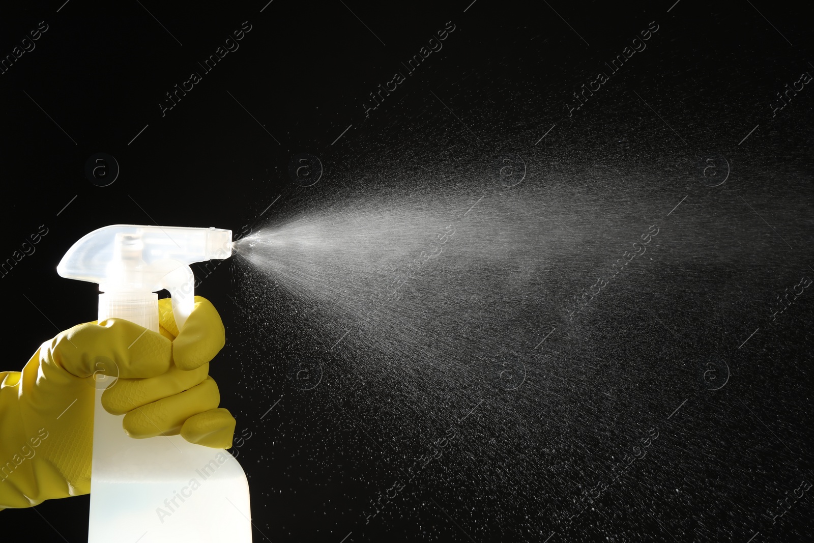 Photo of Woman spraying liquid from bottle on black background, closeup