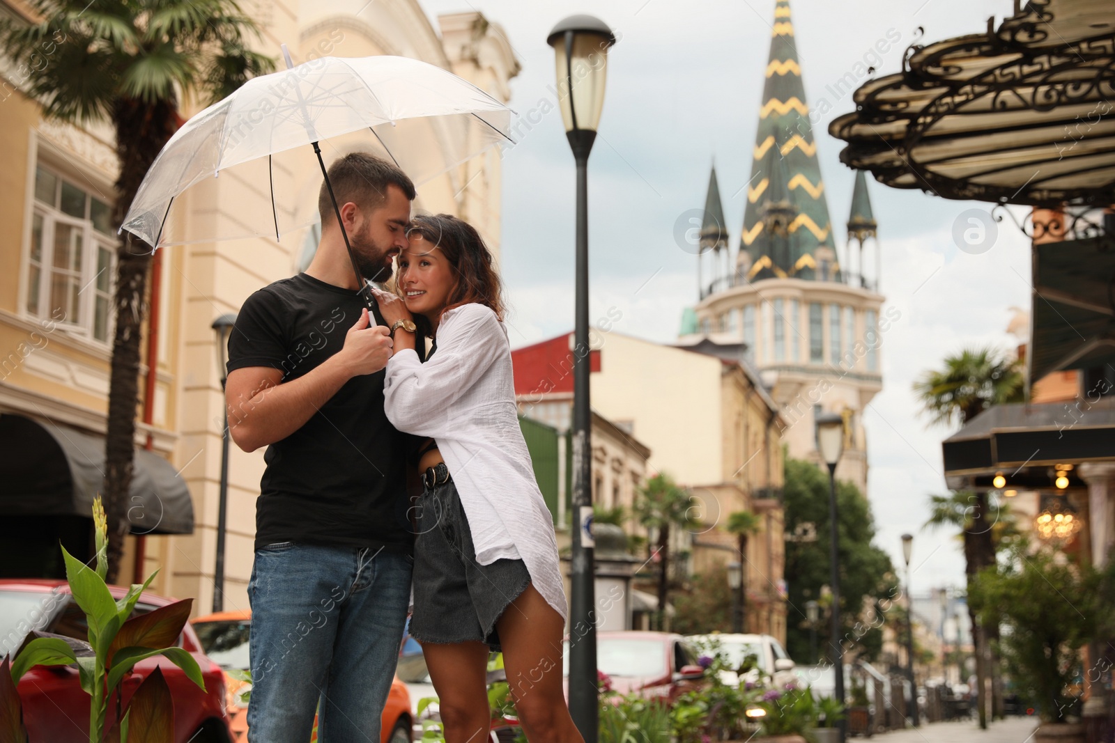 Photo of Young couple with umbrella enjoying time together under rain on city street