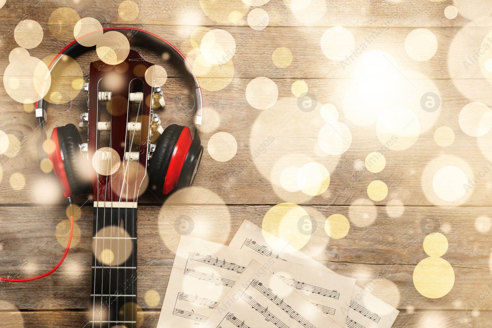 Image of Christmas and New Year music. Headphones, guitar and music sheets on wooden background, bokeh effect
