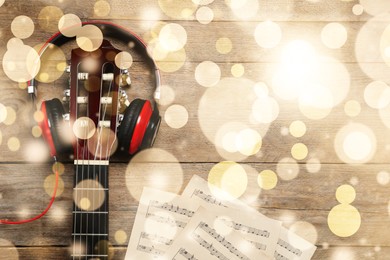 Image of Christmas and New Year music. Headphones, guitar and music sheets on wooden background, bokeh effect