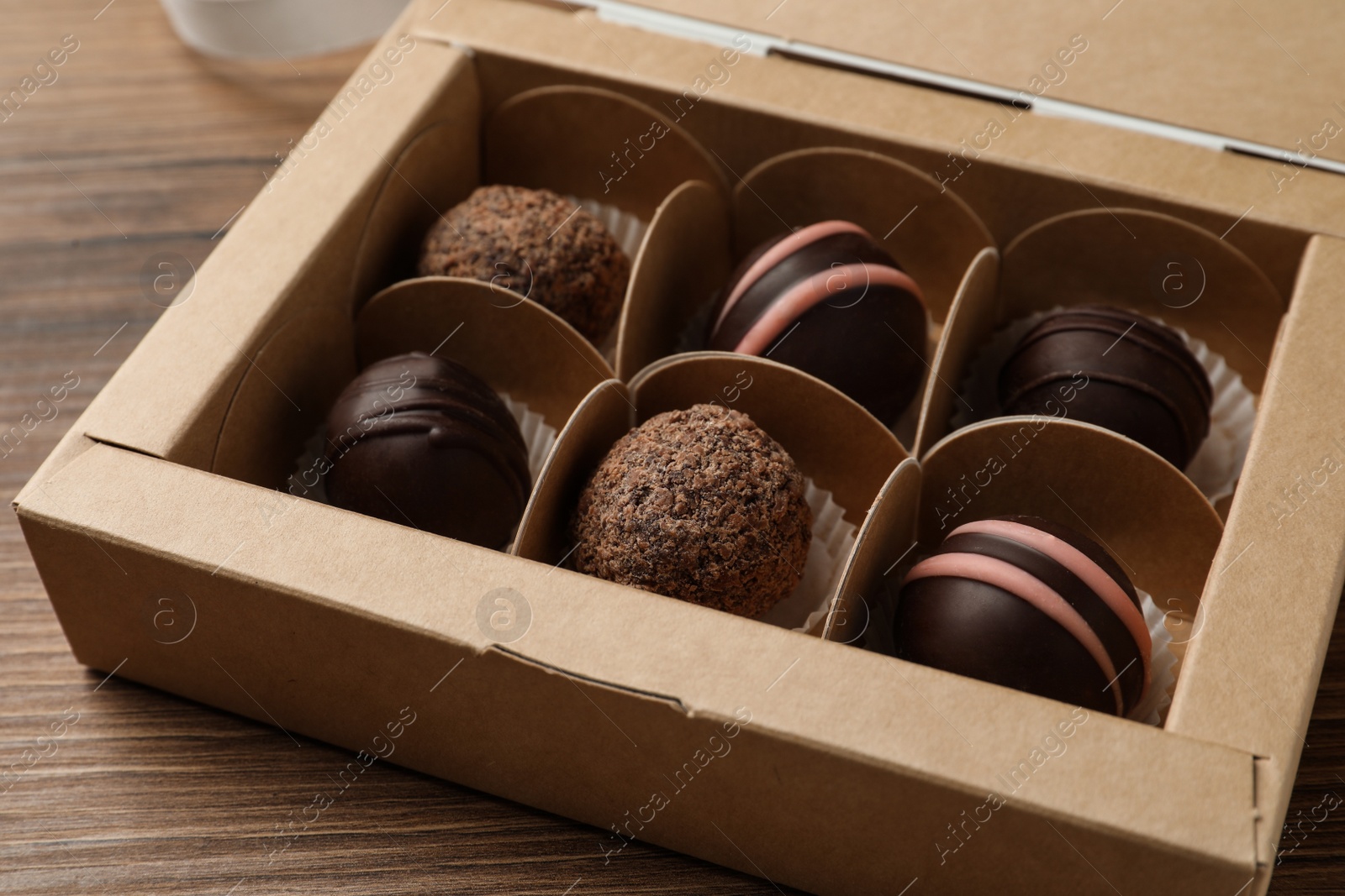 Photo of Many different delicious chocolate truffles in box on wooden table, closeup