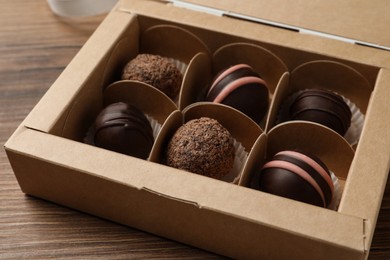 Many different delicious chocolate truffles in box on wooden table, closeup