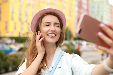 Beautiful young woman in stylish hat taking selfie outdoors