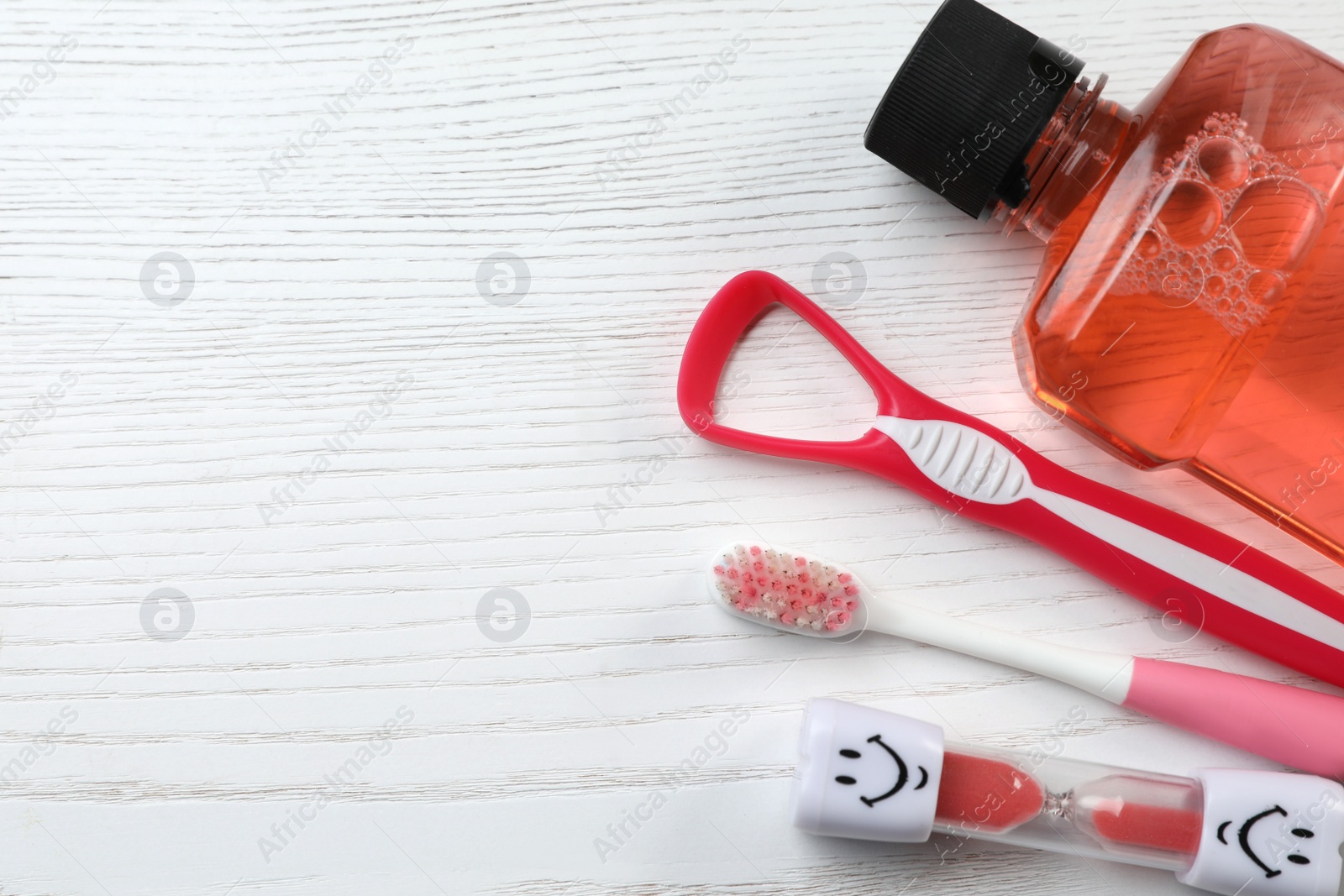 Photo of Tongue cleaner, toothbrush, mouthwash and hourglass on white wooden table, flat lay. Space for text