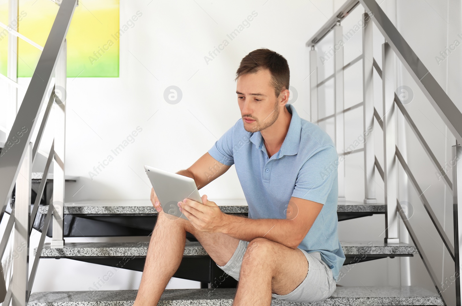 Photo of Young man with tablet sitting on staircase indoors