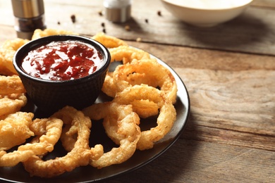 Homemade crunchy fried onion rings with tomato sauce on wooden table, closeup. Space for text