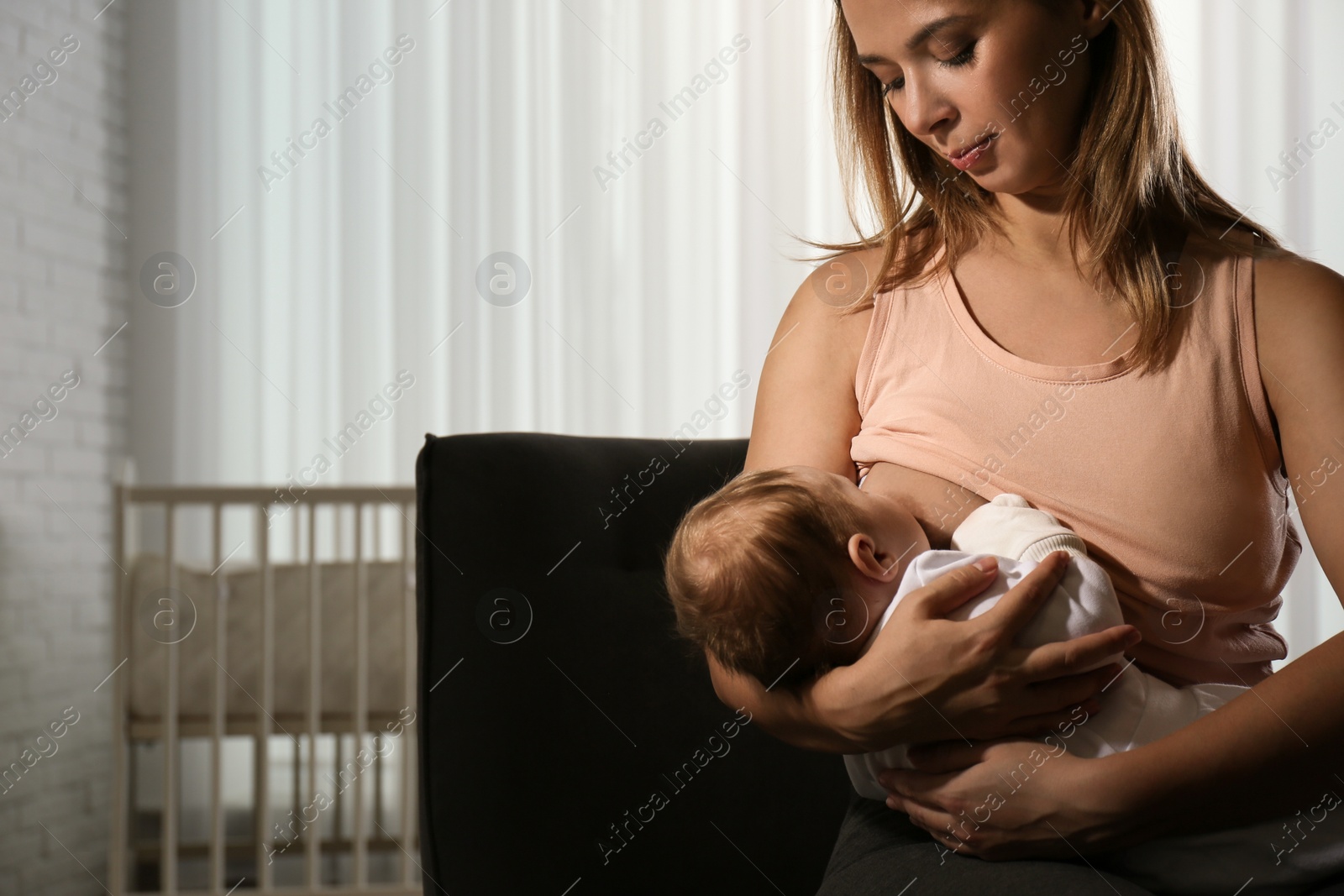 Photo of Young woman breast feeding her little baby at home. Space for text