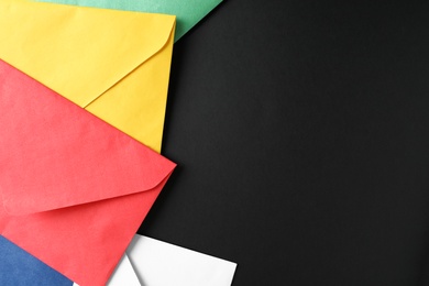 Colorful paper envelopes on black background, flat lay. Space for text