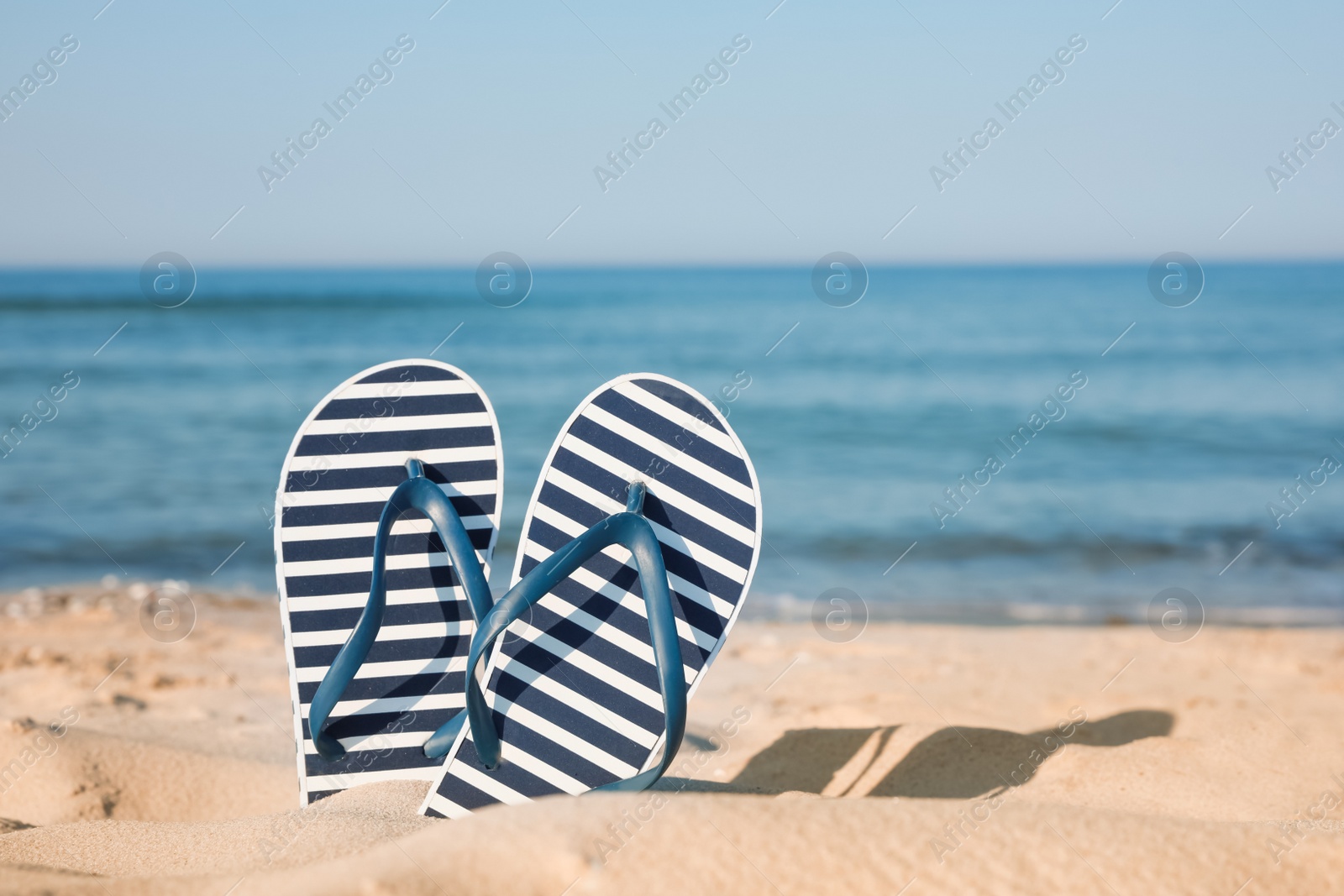 Photo of Pair of stylish flip flops in sand on beach