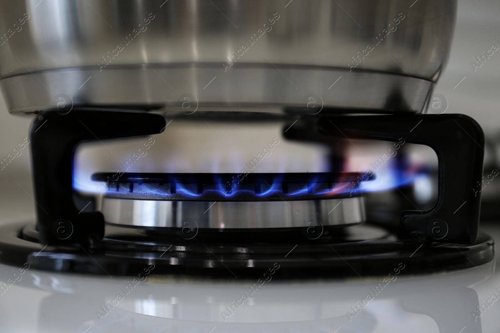 Photo of Pot on modern kitchen stove with burning gas, closeup