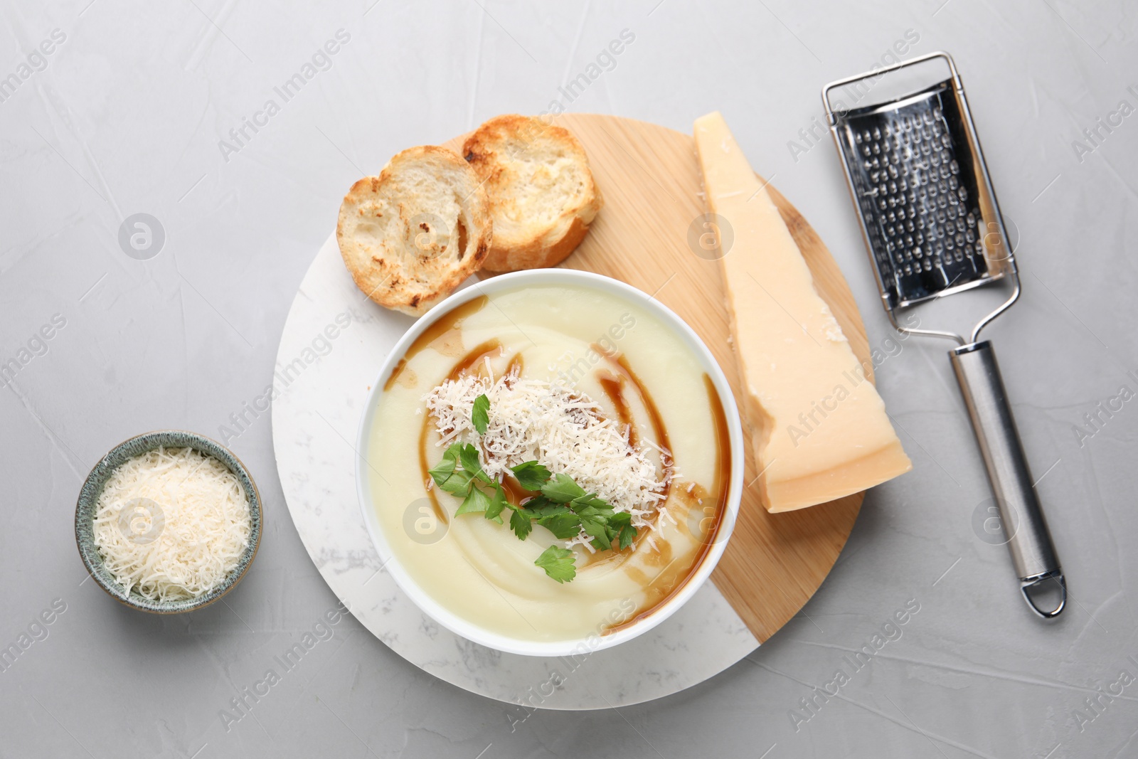 Photo of Delicious cream soup with parmesan cheese, soy sauce in bowl and croutons on light grey table, flat lay