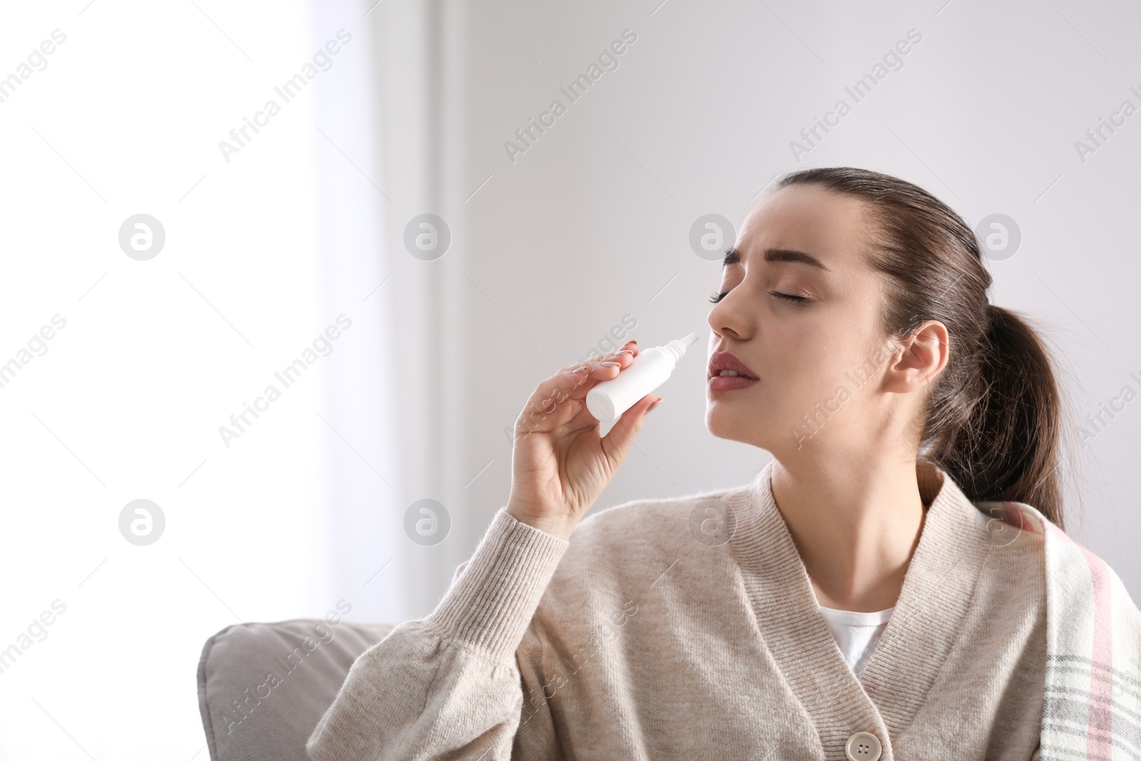 Photo of Sick young woman using nasal spray at home