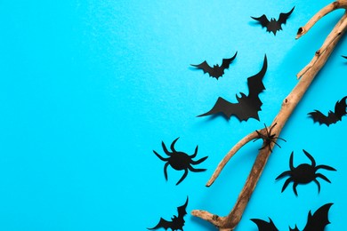 Flat lay composition with paper bats, spiders and wooden branch on light blue background, space for text. Halloween decor