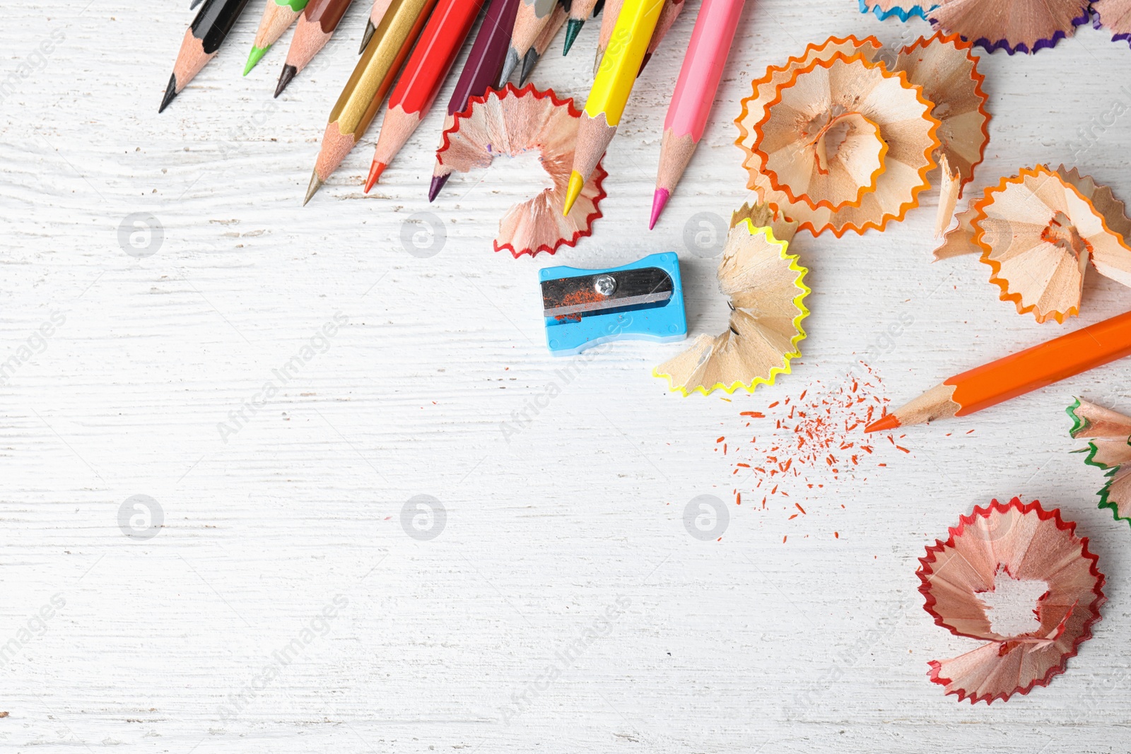 Photo of Color pencils, sharpener and shavings on white wooden table, flat lay. Space for text