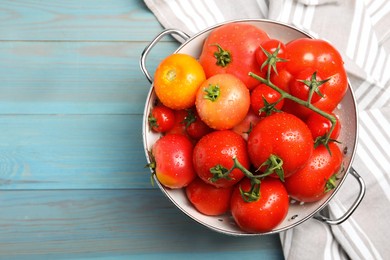 Photo of Many different ripe tomatoes in colander on light blue wooden table, top view. Space for text