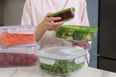 Woman holding containers with different fresh products in kitchen, closeup. Food storage