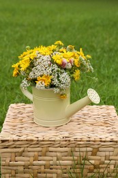 Pale yellow watering can with beautiful flowers on wicker box outdoors