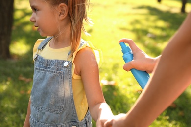 Photo of Mother applying insect repellent onto girl's hand in park, closeup