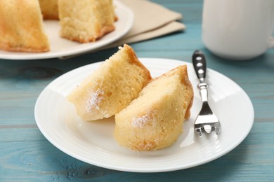 Pieces of delicious sponge cake and fork on light blue wooden table, closeup