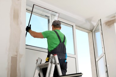 Worker on folding ladder installing window indoors