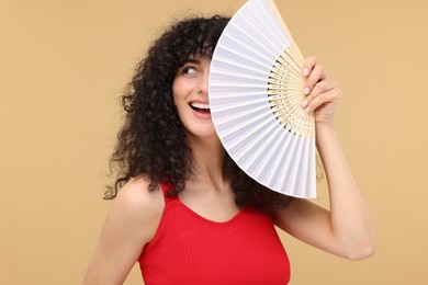 Happy woman holding hand fan on beige background